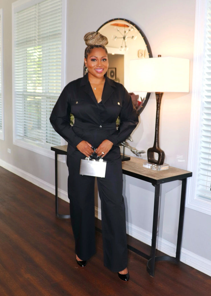 Woman in a black outfit standing in a room with wooden flooring and large windows.