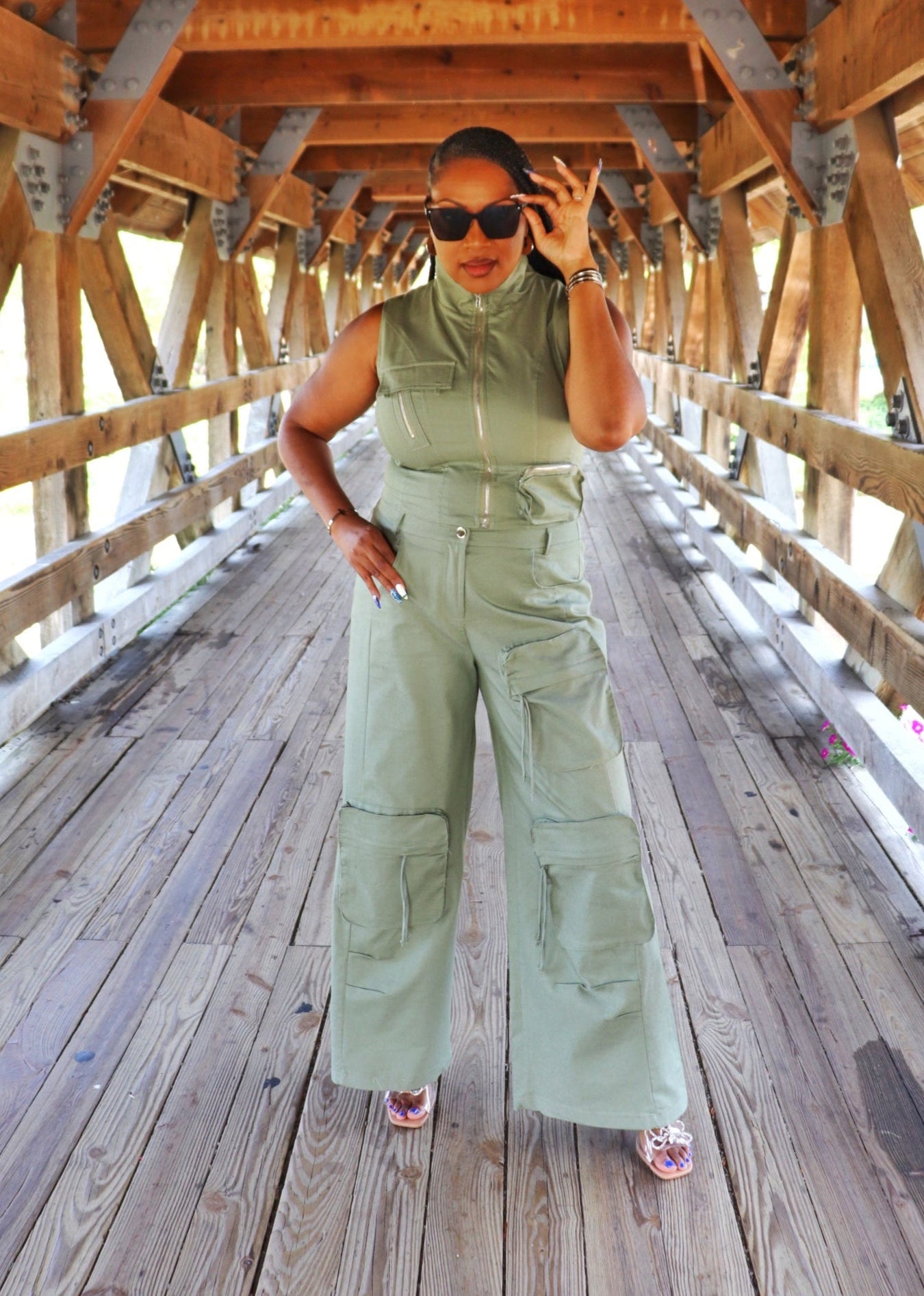 Beautiful Black woman in a green jumpsuit standing on a wooden bridge at the Naperville Riveerwalk bridge