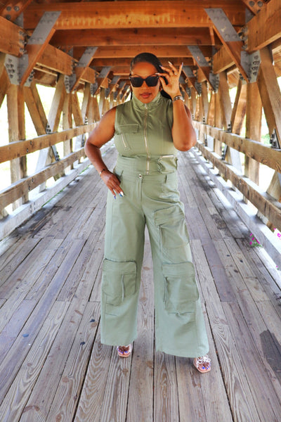Beautiful Black woman in a green jumpsuit standing on a wooden bridge at the Naperville Riveerwalk bridge