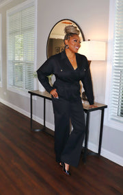 Woman in a black outfit standing in a room with wooden flooring and large windows.