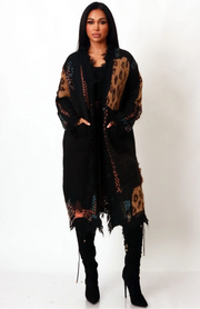 Woman wearing a black leopard distressed longline cardigan with pockets, styled as a coat over black outfit and knee-high boots.