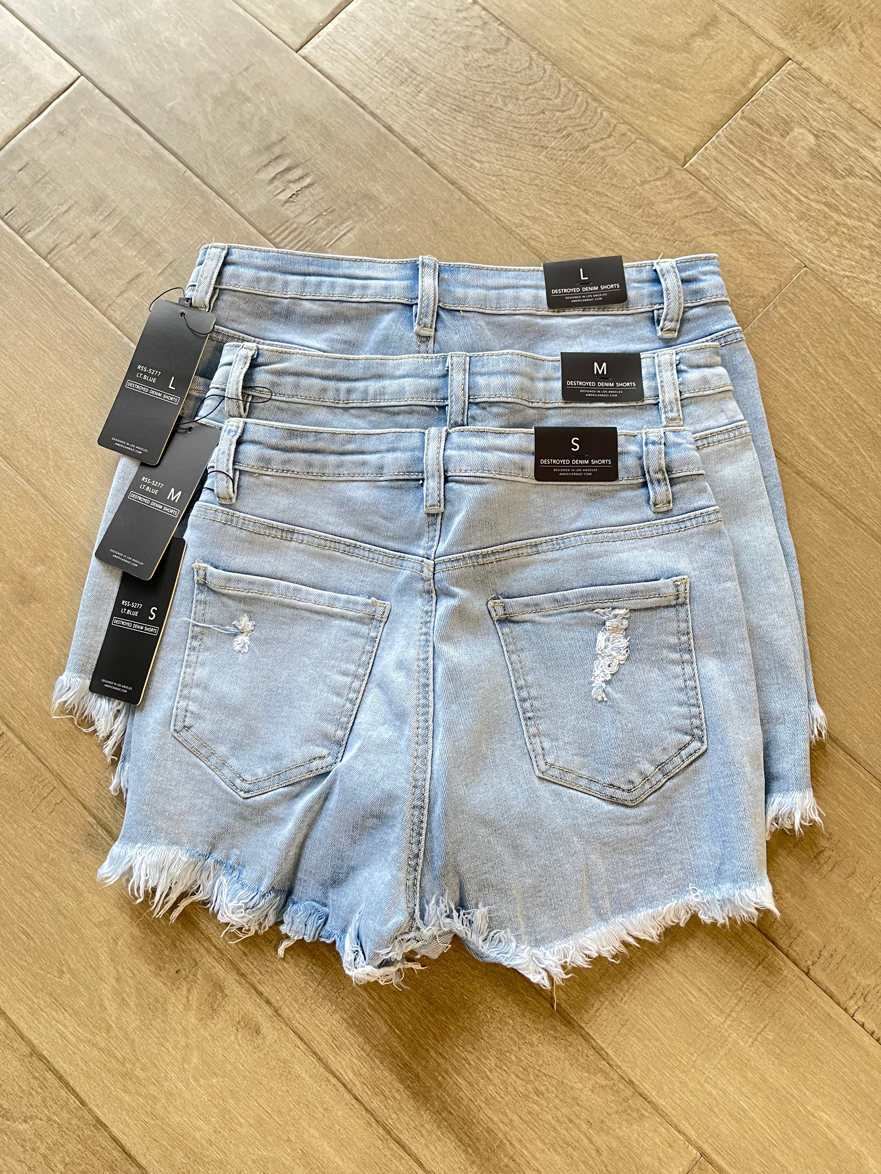 S M L light wash high-waisted denim shorts with raw hem from Adrienne Rebecca Boutique dispayed on a wooden floor
